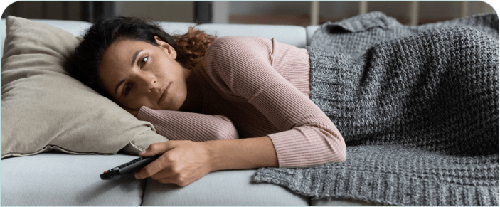 A woman struggling to get to sleep, holding a remote on her couch.